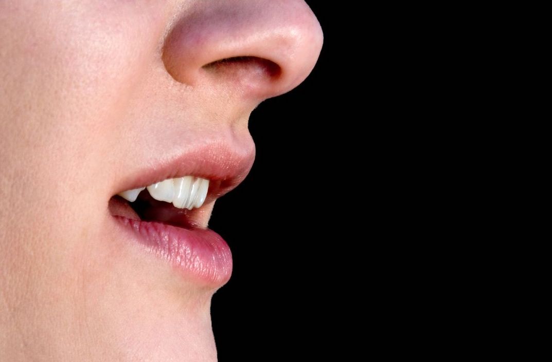 Image of a person's face, showing the nose to chin area. The person's mouth is open.