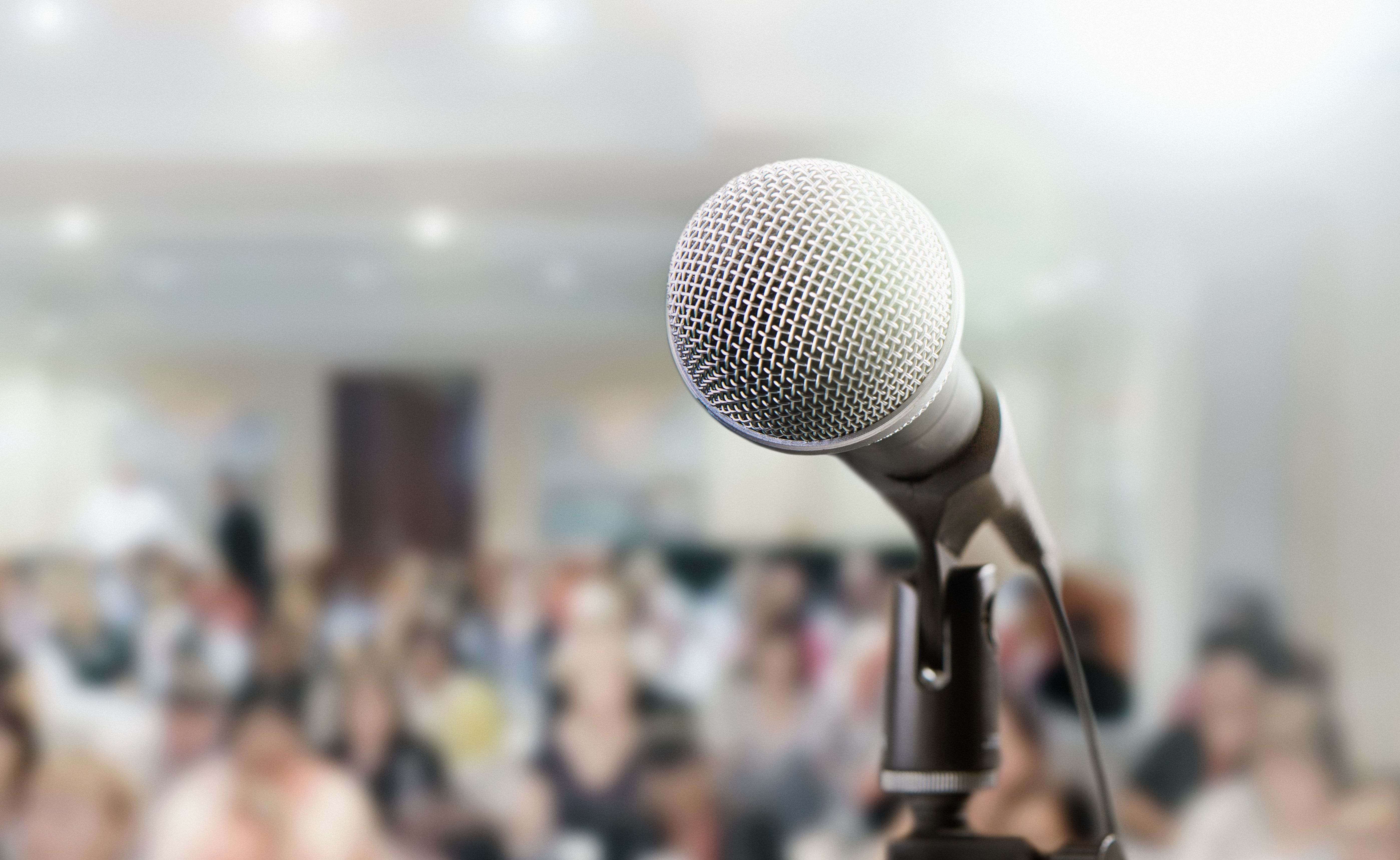Image of a microphone in the foreground of a lecture hall