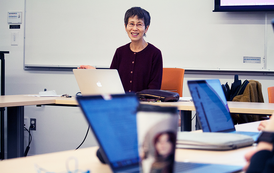 A picture of Professor Ryuko Kubota in class, laughing, sitting in front of a laptop computer