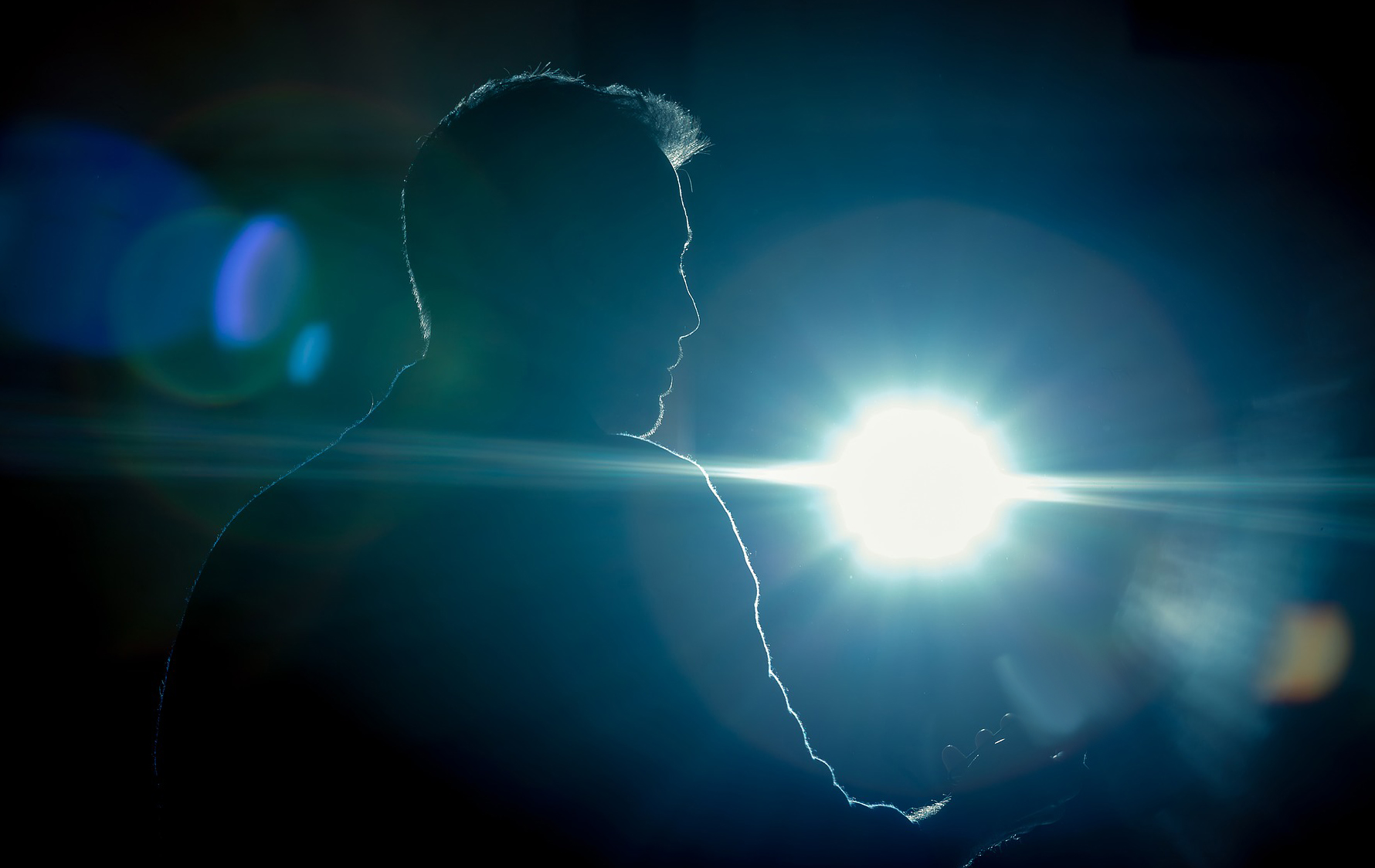 A photo of a mans silhouette, holding a phone, lit up by a spotlight