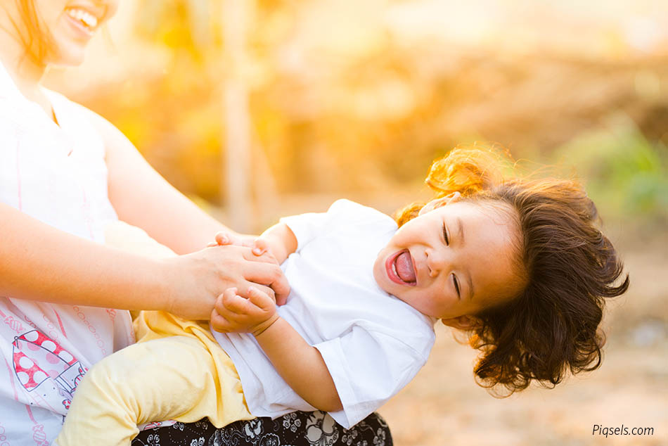 An image of a parent holding a laughing child, who is leaning almost horizontal, with sunlight in the background