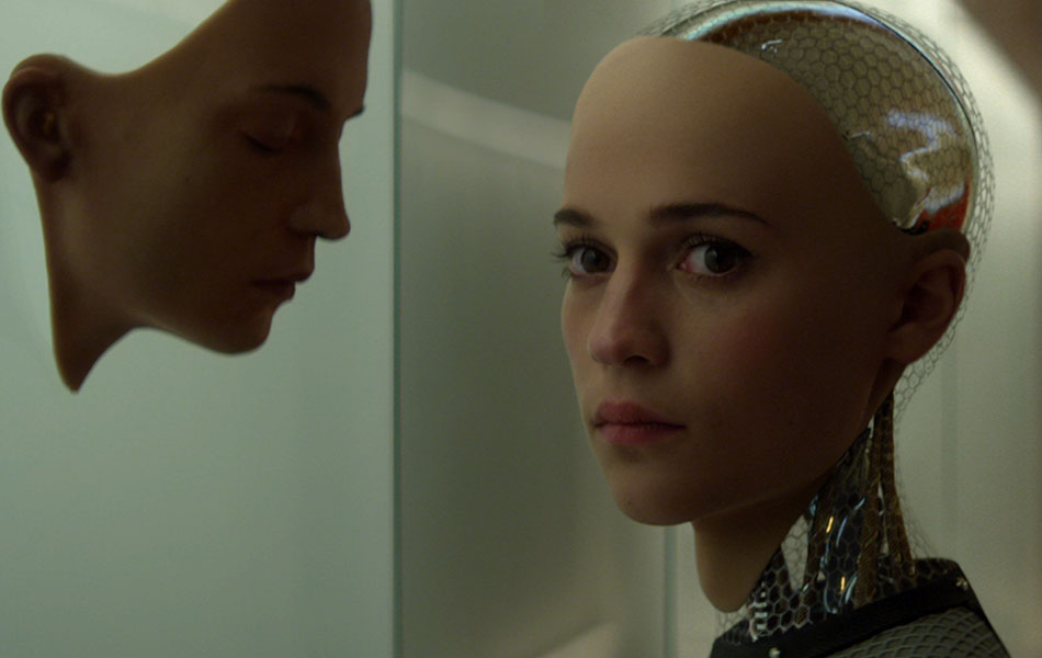 A still from the film of a human mask on a glass wall in front of which Ava the robot stands looking into the camera