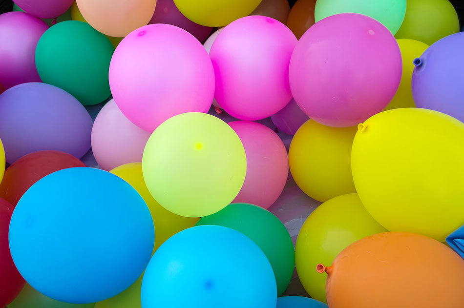 A picture of many different coloured balloons grouped together, including pink, blue, orange, green and yellow balloons.