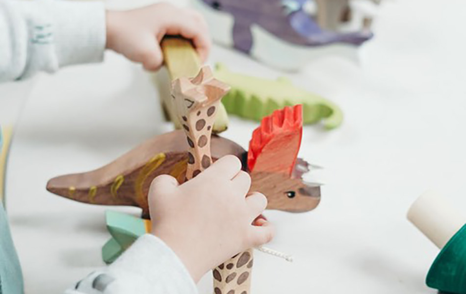 A close up of a child's hands playing with a wooden triceratops and a wooden giraffe
