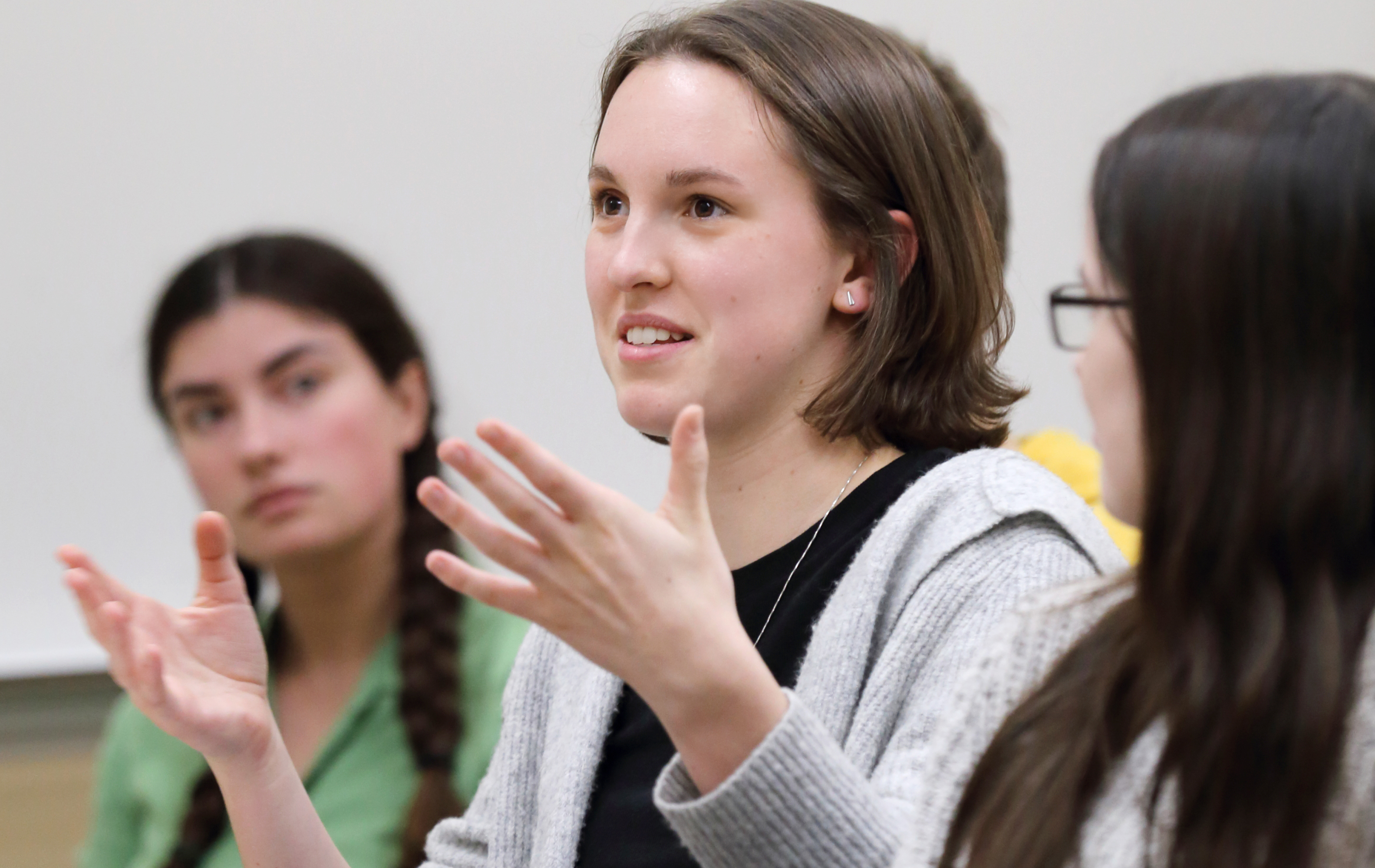 An image of Lauren speaking, gesturing with her hands, while classmates listen to her