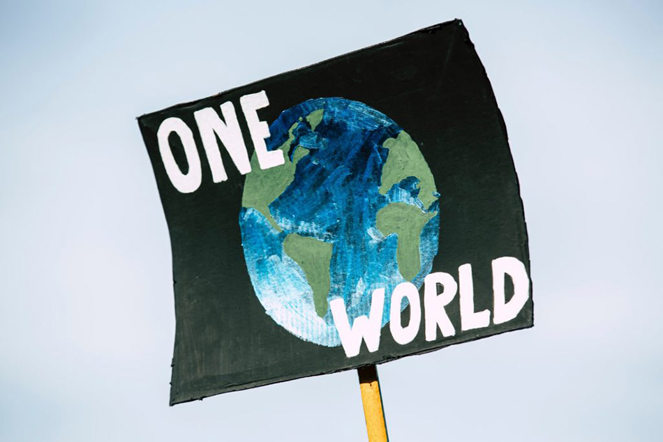 An image of a black poster held up in the sky which reads one world, with a picture of Earth