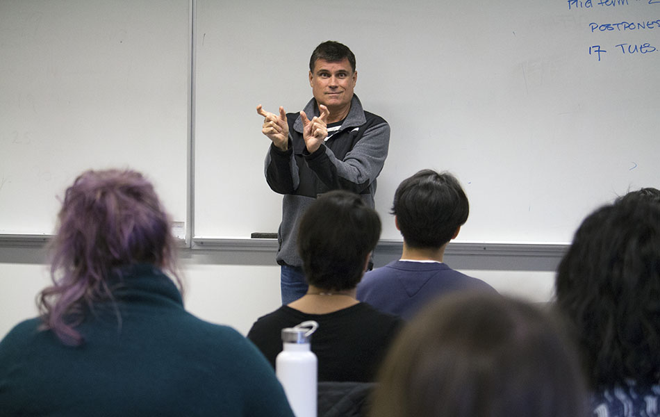 A photo of Nigel Howard standing in front of a class teaching ASL
