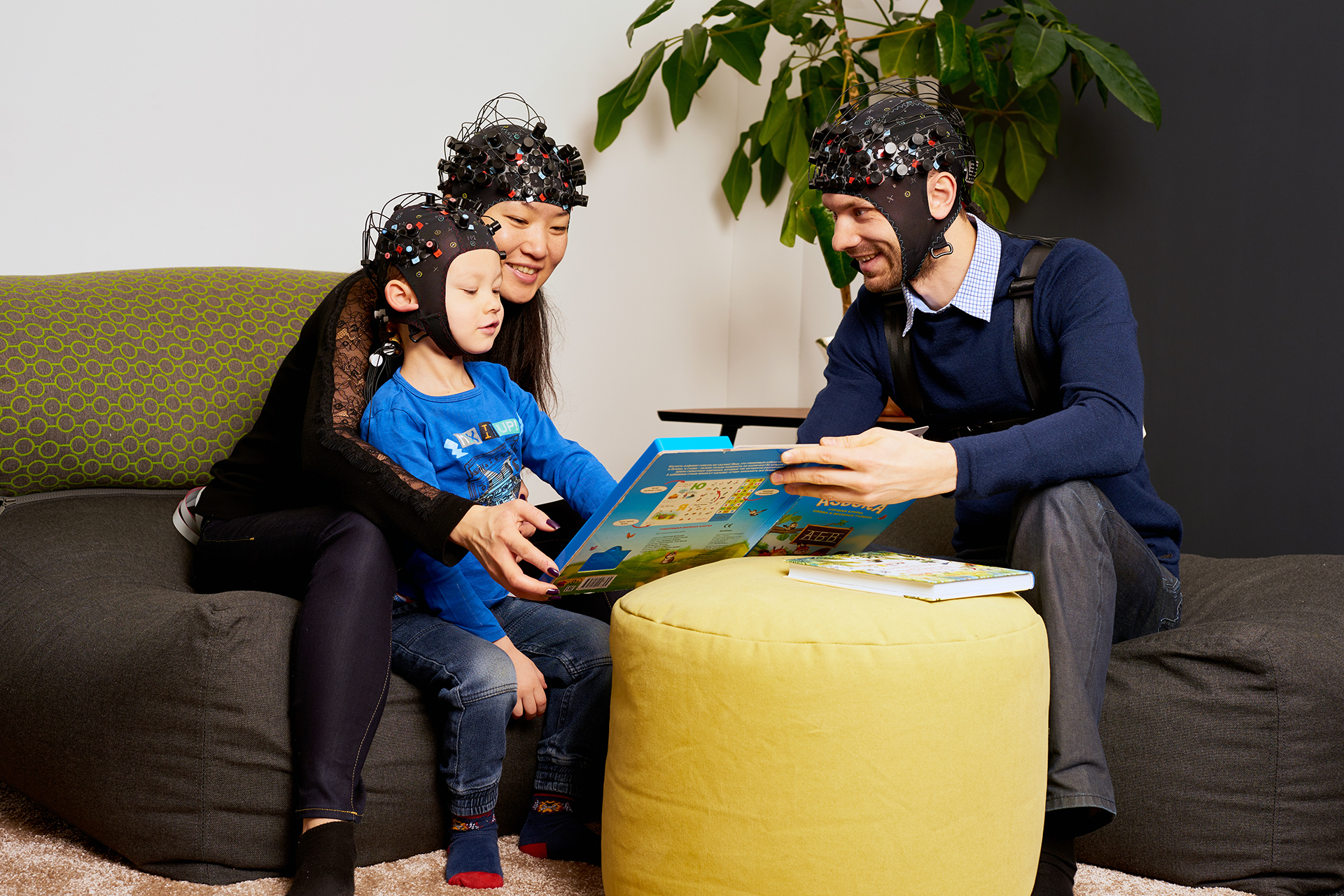 An image of parents reading a book to a child. Everyone is wearing EEG caps.