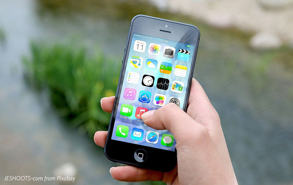 An image of a hand holding an iPhone above the ground, with apps showing on the screen
