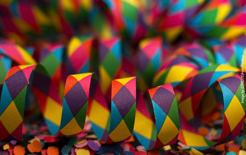 A close up of rainbow coloured confetti tape, sitting in loops on a flat surface