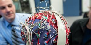 A close up picture of the back of a persons head, who is wearing a red and blue cap covered in electrodes