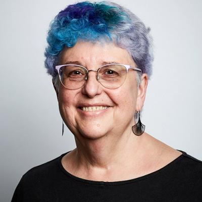 A picture of Professor Catherine Best who is wearing glasses, a black shirt and has blue hair