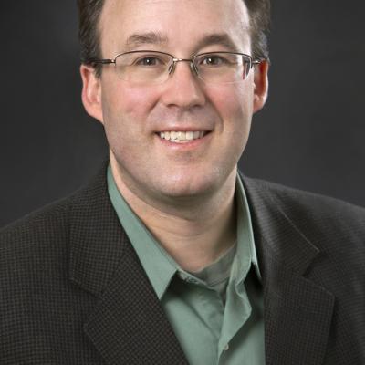 A headshot of Dr Bob McMurray wearing glasses and standing against a black background