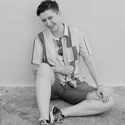 A black and white photo of Bridget Chase sitting against a white wall, laughing.