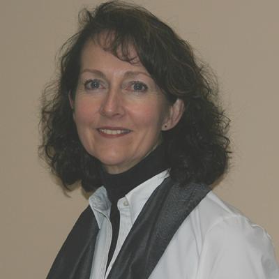 A headshot of Ruth Derksen standing against a brown background