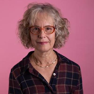 A headshot of Jan Edwards wearing glasses and standing against a pink background