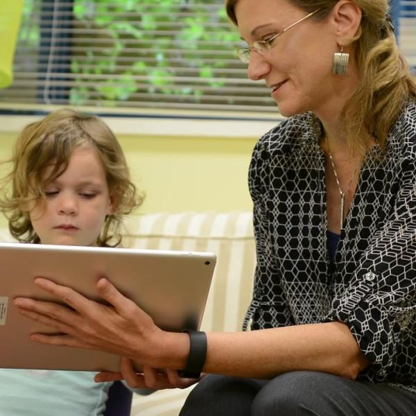 An image of Susan Birch holding an iPad in front of a child