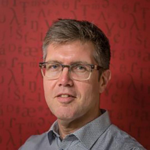 A headshot of Gunnar Hansson wearing glasses and standing against a red background