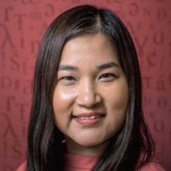 A headshot of Zoe Lam with shoulder length hair, standing against a red background