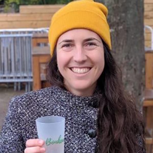 A headshot of Marie-Eve Bouchard holding a glass and wearing a yellow toque